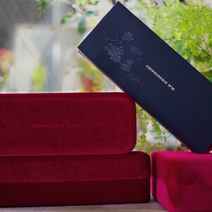 May include: Three red velvet boxes with the text "Chinoiserie N&deg;19" embossed on the top box. The boxes are stacked on top of each other.