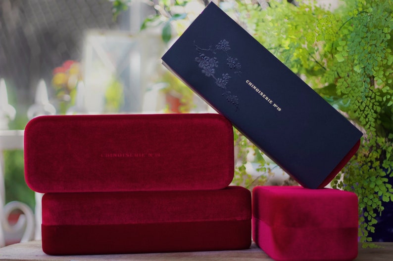 May include: Three red velvet boxes with the text "Chinoiserie N&deg;19" embossed on the top box. The boxes are stacked on top of each other.