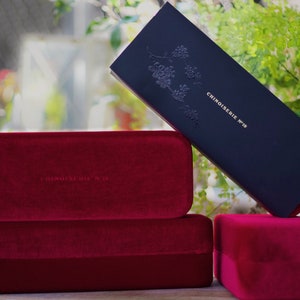 May include: Three red velvet boxes with the text "Chinoiserie N&deg;19" embossed on the top box. The boxes are stacked on top of each other.