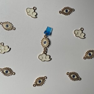 Puede incluir: Surtido de dijes de tono dorado con nubes blancas y ojos azules malvados. Los dijes son perfectos para agregar un toque de fantasía y protección a los proyectos de joyería.