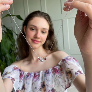 May include: A silver necklace with a butterfly pendant featuring red gemstones. The butterfly has intricate details and is a delicate piece of jewellery.