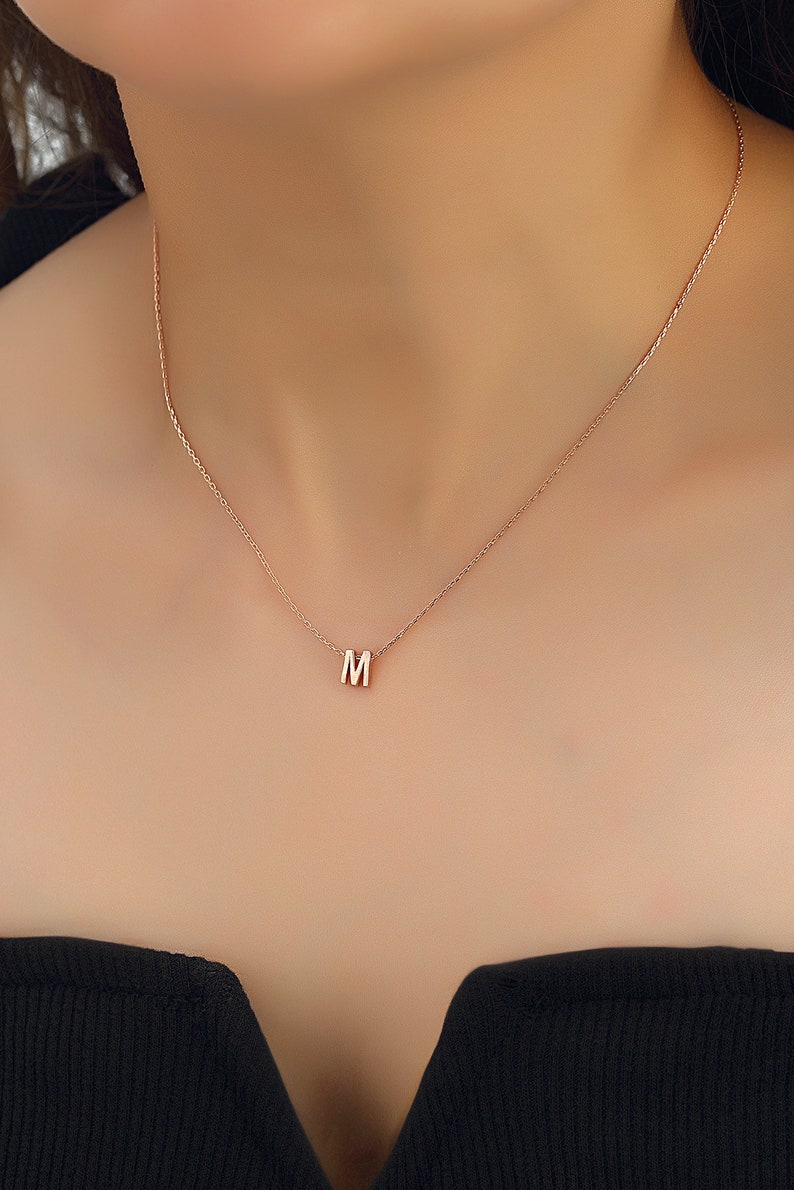 May include: A delicate gold chain necklace with a small letter 'M' pendant.