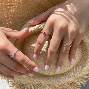 May include: Two gold rings with oval-shaped red gemstones. The rings are worn on the fingers of a person's hand.