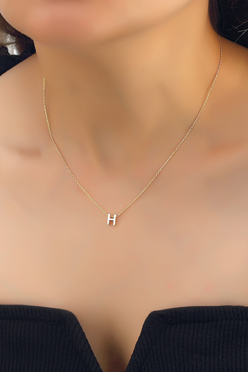 May include: A gold chain necklace with a small letter H pendant.
