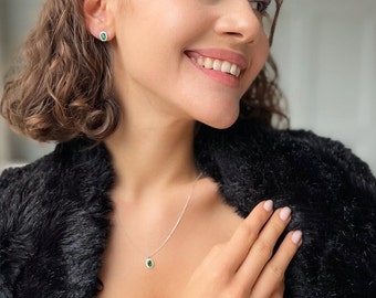 May include: A woman wearing a black fur jacket with a silver necklace and bracelet featuring green oval stones. She is also wearing matching green oval stud earrings.