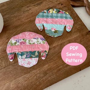 Peut inclure: Deux dessous de verre en tissu faits à la main avec un motif patchwork, présentant des motifs floraux et rayés en rose, vert et bleu. Les dessous de verre sont sur une planche à découper en bois. Un cercle rose avec le texte "PDF Sewing Pattern" est dans l'image.