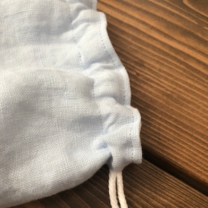 May include: A light blue fabric drawstring bag with white drawstrings. The bag is made of a soft, textured fabric.