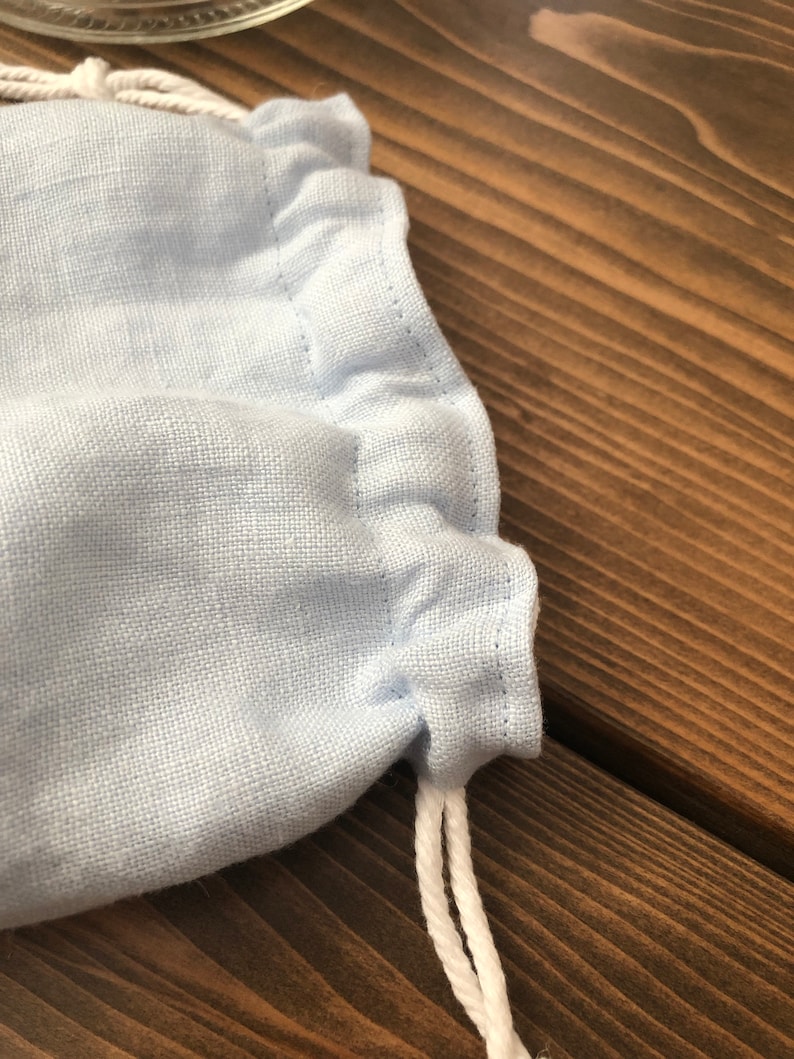 May include: A light blue fabric drawstring bag with white drawstrings. The bag is made of a soft, textured fabric.