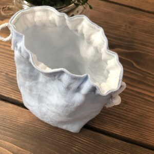 May include: A light blue drawstring bag with a white lining. The bag is made of a soft, textured fabric and has a gathered top.