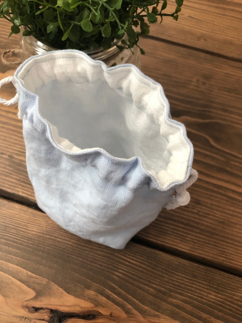 May include: A light blue drawstring bag with a white lining. The bag is made of a soft, textured fabric and has a gathered top.