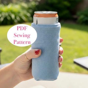 May include: A pale blue drinks can cooler holding a beverage can. The cooler is made of a soft, textured material. The text "PDF Sewing Pattern" is in a white circle. The background is a blurred outdoor scene.