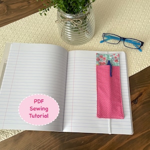 May include: A pink and white polka dot fabric pen holder with a floral fabric lining. The pen holder is laying open on a notebook with the text "PDF Sewing Tutorial" on the page.