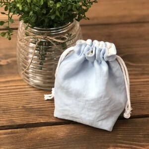 May include: A light blue linen drawstring bag with white lining and white drawstrings. The bag is sitting on a wooden surface.