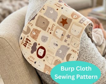 May include: A beige burp cloth with a repeating pattern of cartoon bears, stars, and text. The text includes phrases like "Little Man" and "Big Bear". The cloth is curved and has a blue oval with the text "Burp Cloth Sewing Pattern".