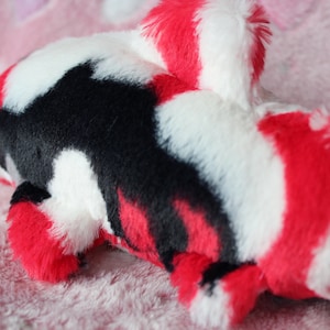 Puede incluir: Un juguete de peluche de pez koi en rojo, negro y blanco. El peluche tiene una textura suave y peluda y un dise&ntilde;o detallado, incluyendo aletas y cola. El juguete est&aacute; dise&ntilde;ado para parecerse a un pez koi.