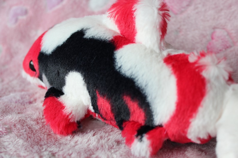 Puede incluir: Un juguete de peluche de pez koi en rojo, negro y blanco. El peluche tiene una textura suave y peluda y un dise&ntilde;o detallado, incluyendo aletas y cola. El juguete est&aacute; dise&ntilde;ado para parecerse a un pez koi.