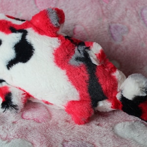 Puede incluir: Un juguete de peluche con forma de pez koi en rojo, negro, blanco y gris. El juguete blando tiene un dise&ntilde;o estampado y est&aacute; sobre una superficie rosa con estampado de corazones. El juguete est&aacute; dise&ntilde;ado para parecerse a un pez koi.