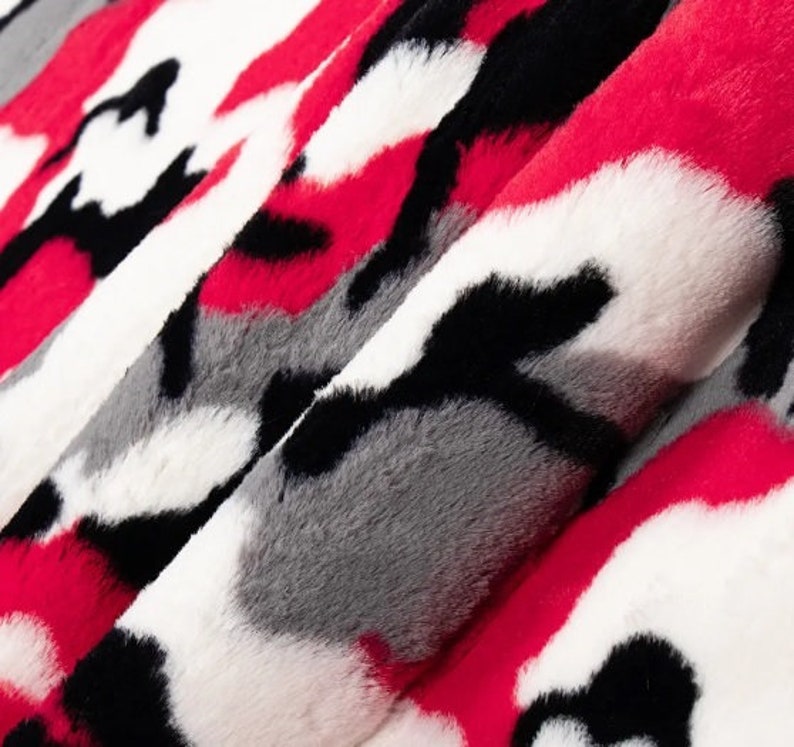 Puede incluir: Primer plano de una tela estampada con un dise&ntilde;o de camuflaje. El textil presenta una mezcla de colores rojo, negro, blanco y gris. El material suave y afelpado est&aacute; doblado, revelando la textura y las variaciones de color.