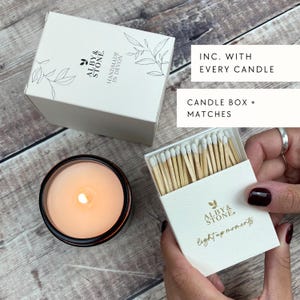 a person holding a box of matches next to a lit candle in a glass container, with a hand holding a box of matches.
