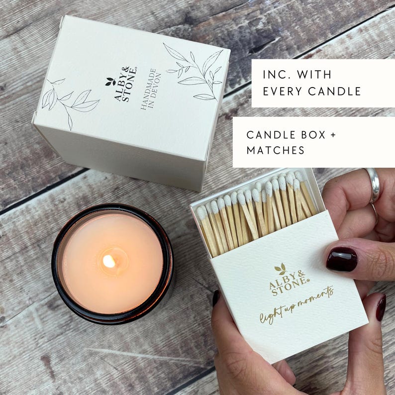 a person holding a box of matches next to a lit candle in a glass container, with a hand holding a box of matches.