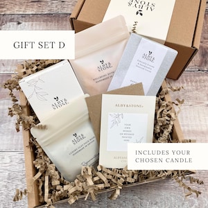 A gift set containing a box of ALBY & STONE bath products, a card, and a candle, all neatly arranged in a cardboard box with shredded paper.