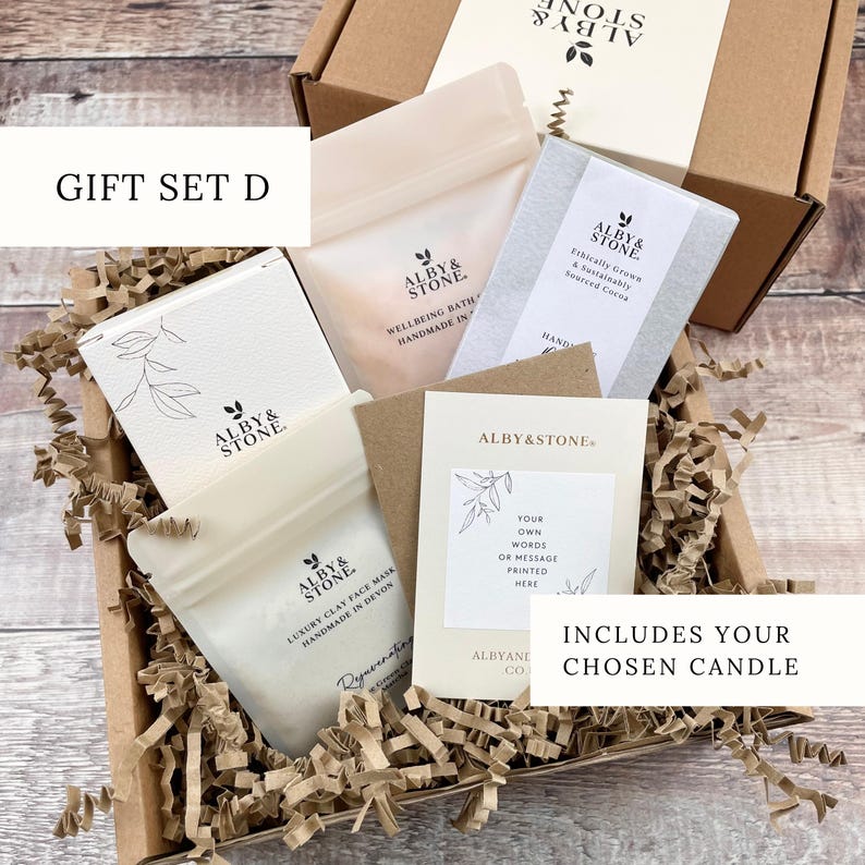 A gift set containing a box of ALBY & STONE bath products, a card, and a candle, all neatly arranged in a cardboard box with shredded paper.
