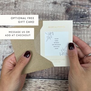 a person's hands holding a gift card and a card with instructions for using the card. The card has a message that allows the recipient to add their own words or message, and the card is from Alby & Stone.