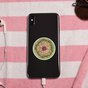 May include: A black smartphone with a green, yellow, and red circular sticker on the back. The sticker features a detailed design of a flower with multiple petals.