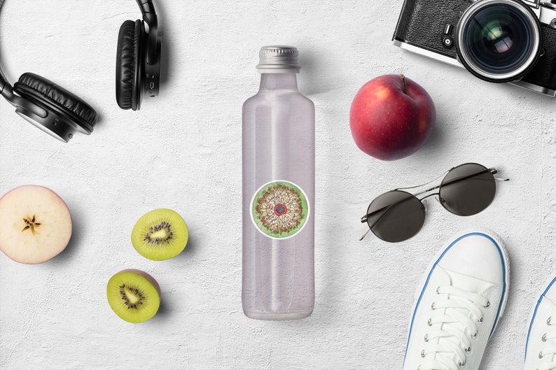 May include: A clear glass water bottle with a silver lid and a round sticker with a colorful mandala design. The bottle is surrounded by various items, including headphones, sunglasses, a kiwi fruit, an apple, and a pair of white sneakers.