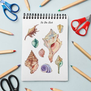 Pode incluir: Um caderno branco de espiral com as palavras "To Do List" escritas na capa. O caderno está rodeado de lápis de cor, tesouras e ilustrações de aquarela de conchas.