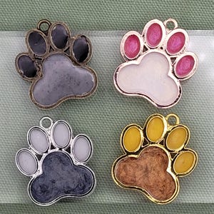 May include: Four different colored paw print charms. The charms are made of metal with a resin fill. The colors are gray, white, yellow, and pink.
