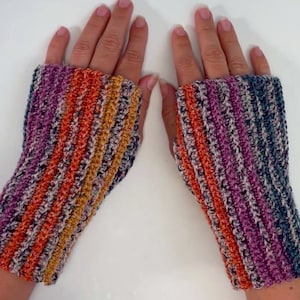Könnte beinhalten: Ein Paar gestreifte Fingerlose Handschuhe in den Farben Lila, Orange und Grau. Die Handschuhe sind mit einem glitzernden Garn gehäkelt.