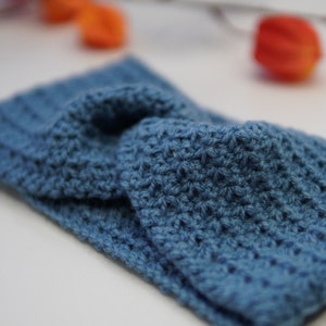 May include: A blue crocheted headband with a knotted design. The headband is made with a soft, textured yarn.