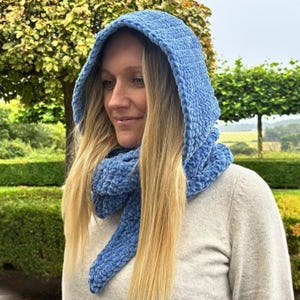 Peut inclure: Une écharpe à capuche bleu clair fabriquée à partir d'un fil épais, doux et semblable à du velours. L'accessoire présente une capuche profonde qui se prolonge en une longue écharpe enveloppante avec un motif en tricot texturé et épais.