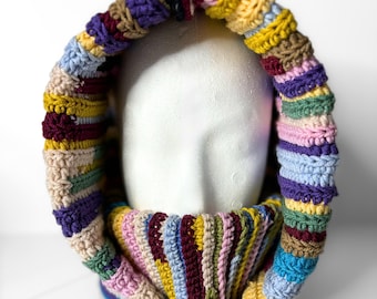 May include: A colorful crocheted cowl with a striped pattern in shades of purple, blue, green, yellow, pink, and brown. The cowl is folded over and has a hood.