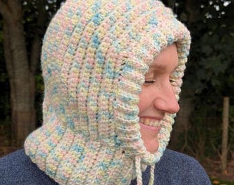 May include: A pastel-colored crochet hood with a drawstring closure. The hood is made of soft yarn in shades of cream, pink, blue, and yellow. The ribbed texture adds visual interest. This handmade hood is perfect for cool weather.