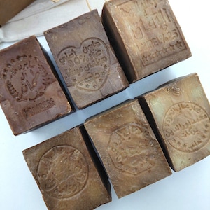 Puede incluir: Un conjunto de barras de jabón rectangulares de color marrón con texto y diseños árabes en relieve. Algunas barras presentan la palabra "PRINCESS" y símbolos en forma de estrella. Los jabones tienen un aspecto rústico y natural.