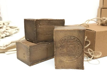 May include: Three bars of brown soap with a circular stamp in Arabic script. The soap is wrapped in brown paper and tied with twine.