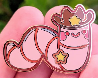 Puede incluir: Un gusano rosa de dibujos animados que lleva un sombrero de vaquero marrón con una estrella amarilla. El gusano tiene una estrella amarilla en su cuerpo y una cara feliz.