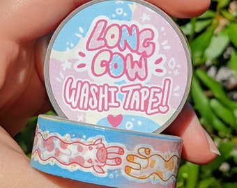 May include: A pink and blue washi tape dispenser with the text "Long Cow Washi Tape!" on the front. The tape features a pink and blue cow print.