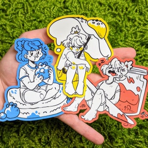 May include: Three colorful stickers featuring cartoon characters. The first sticker shows a blue-haired character sitting on a blue and white donut. The second sticker shows a yellow-haired character sitting with a yellow umbrella. The third sticker shows a character with brown hair sitting on a red and white jar.