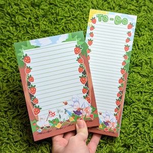 May include: Two lined notepads with a strawberry and forest theme. One notepad has the text "To-Do" at the top and the other has a cartoon illustration of ghosts and a forest scene.
