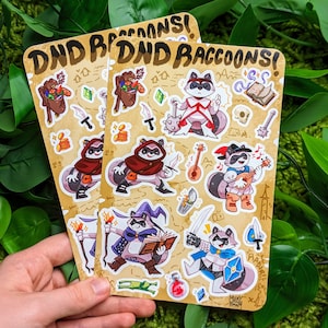 May include: A set of 10 colorful stickers featuring raccoons dressed as Dungeons and Dragons characters. The stickers are printed on a light brown background with the text "DND Raccons!" at the top.