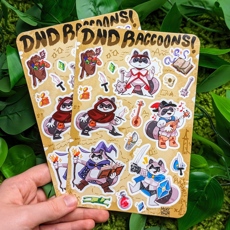 Może przedstawiać: Zestaw 10 kolorowych naklejek przedstawiających szopy pracze przebrane za postacie z Dungeons and Dragons. Naklejki są wydrukowane na jasnobrązowym tle z tekstem "DND Raccons!" u g&oacute;ry.