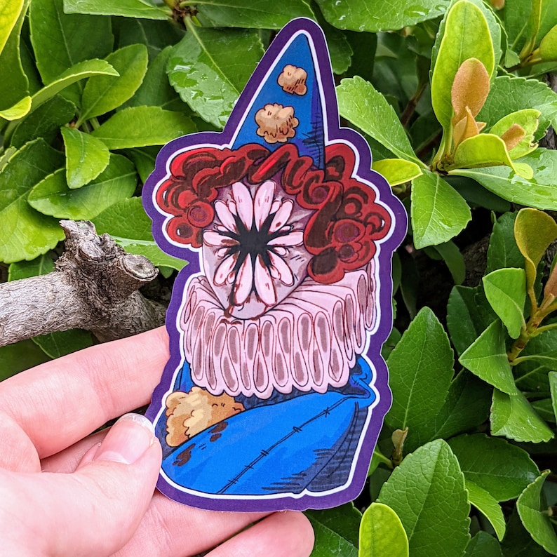 May include: A sticker of a clown with a large, pink flower for a face. The clown is wearing a blue and white hat with a red and white ruffle collar. The clown is holding a small, brown teddy bear.