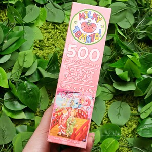 May include: A pink box for a 500-piece jigsaw puzzle featuring a cartoon tomato with the words "Milky Tomato!"  The puzzle is 19.5 inches by 25.25 inches.