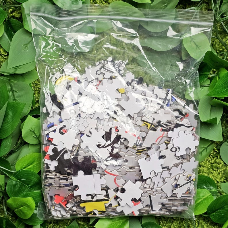 May include: A plastic bag filled with a jumbled pile of colourful jigsaw puzzle pieces. The pieces are mostly white with black, red, yellow, and blue accents.
