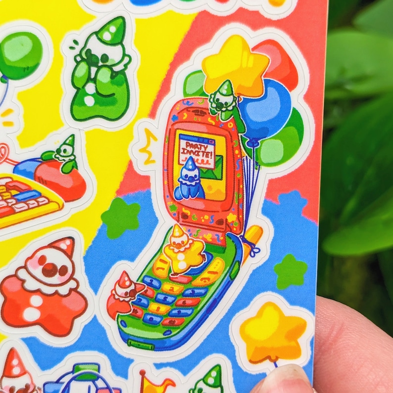 May include: A sticker sheet with a cartoon illustration of a flip phone with a party invite on the screen. The phone is surrounded by stars, balloons, and clowns. The text on the screen reads "Party Invite!"