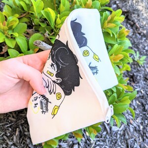 May include: A white zippered pouch with a black and yellow illustration of two people hugging. The illustration includes the text "8:88".
