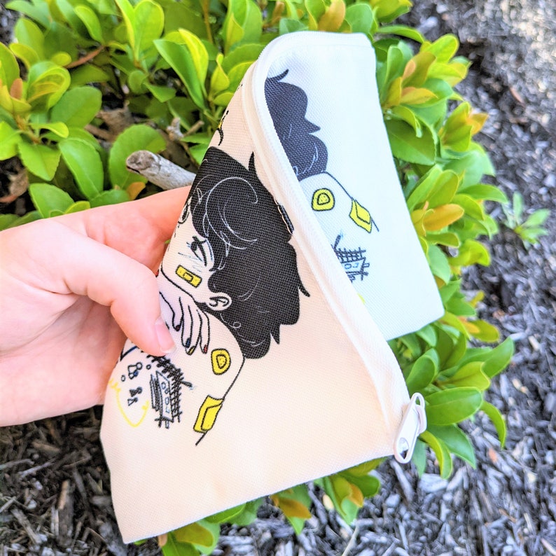 May include: A white zippered pouch with a black and yellow illustration of two people hugging. The illustration includes the text "8:88".